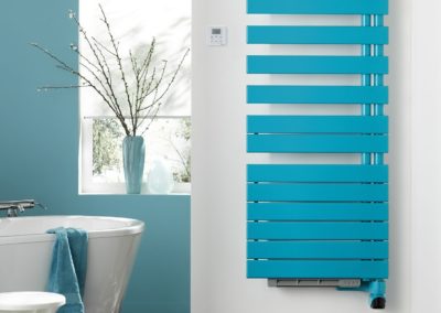 sèche serviette bleu sur un mur blanc avec baignoire en arrière plan dans une salle de bain aux murs bleus