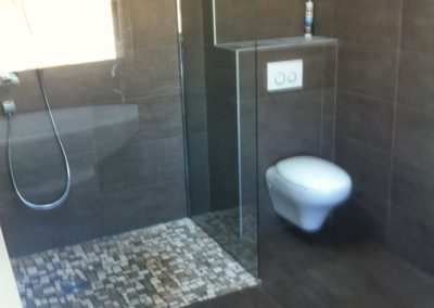 Douche à l'italienne, avec sol en mosaïques, et paroi transparente, toilettes à droite et carrelage gris foncé Manu Casier Thonon