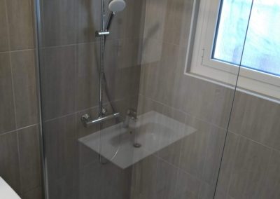 Douche à l'italienne avec pommeau de douche type pluie et une douchette fixée au mur. Paroi de douche transparente